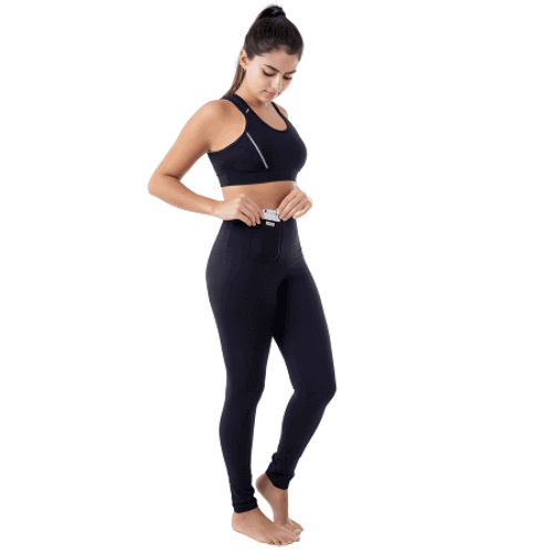 Mulher com a perna levemente levantada e com um top colocando um iphone 6s no bolso de uma legging